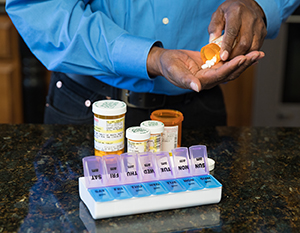 Closeup of man's hands filling pill organizer with medications.