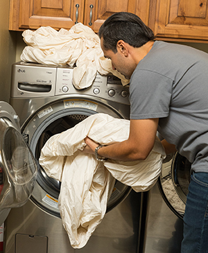 Man loading sheets into home washing machine.