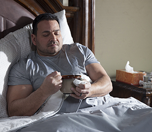 Hombre que toma un plato de sopa en la cama.