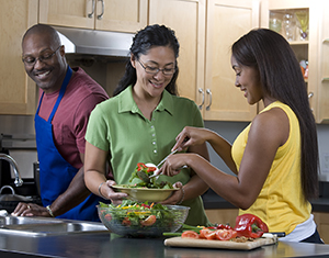 Una familia preparando una ensalada en la cocina.